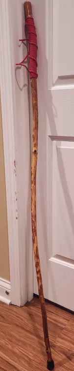 a wooden walking stick with a paracord handle and rubber cane tip